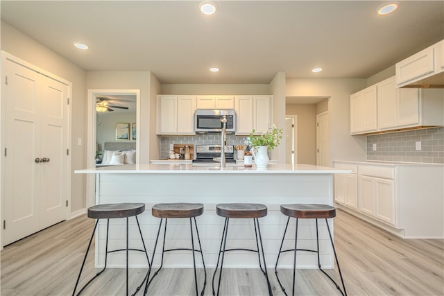 kitchen with white cabinets, tasteful backsplash, an island with sink, and appliances with stainless steel finishes