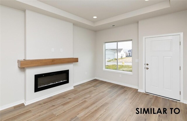 unfurnished living room with light hardwood / wood-style flooring and a raised ceiling