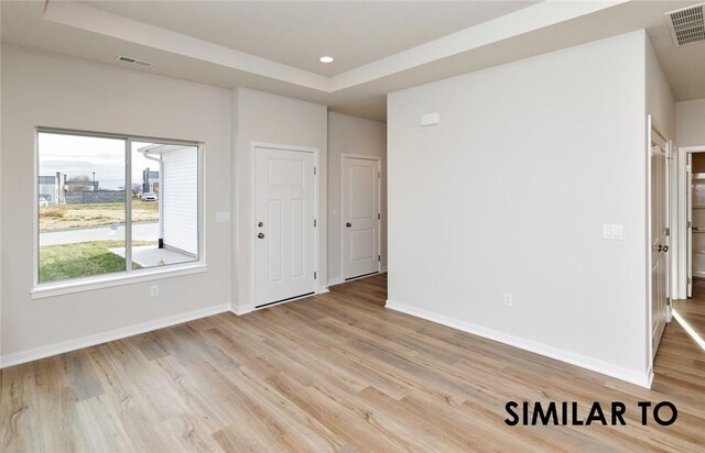 empty room featuring a tray ceiling and light hardwood / wood-style floors