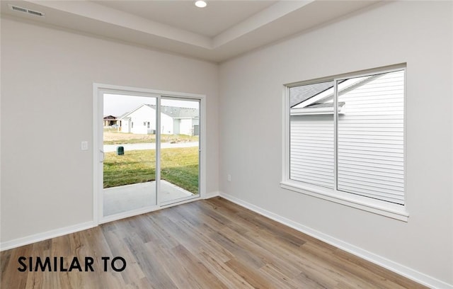 empty room featuring a tray ceiling and light hardwood / wood-style flooring