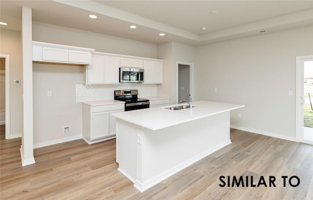 kitchen with sink, appliances with stainless steel finishes, white cabinetry, light hardwood / wood-style floors, and an island with sink