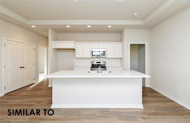 kitchen featuring a kitchen island with sink, stainless steel appliances, tasteful backsplash, white cabinets, and light wood-type flooring