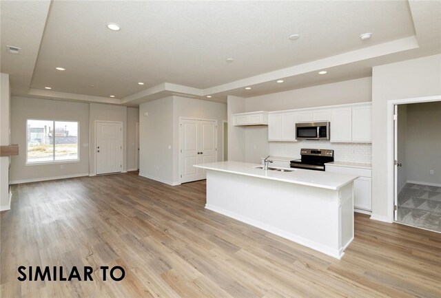 kitchen featuring a raised ceiling, light hardwood / wood-style flooring, appliances with stainless steel finishes, an island with sink, and white cabinets