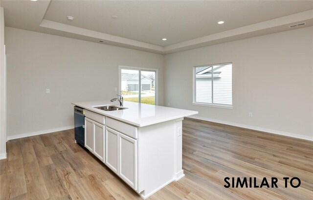 kitchen featuring a kitchen island with sink, light wood-type flooring, white cabinetry, sink, and stainless steel dishwasher