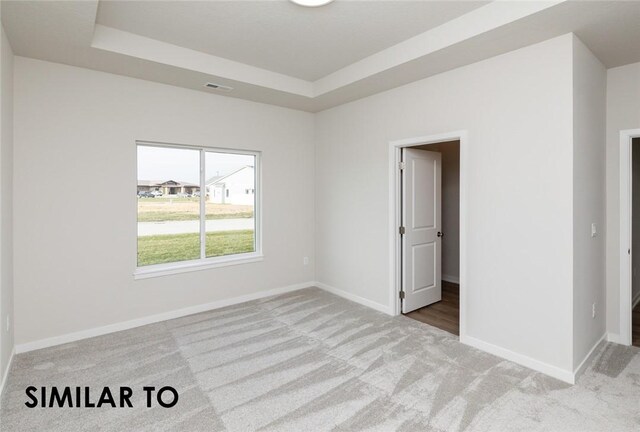 carpeted empty room with a raised ceiling