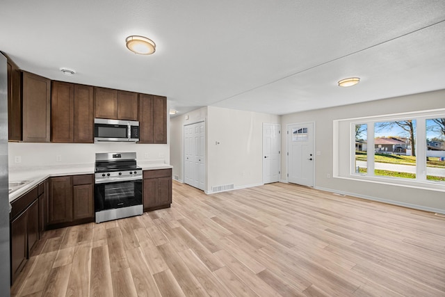 kitchen featuring a textured ceiling, dark brown cabinetry, light wood-type flooring, and stainless steel appliances