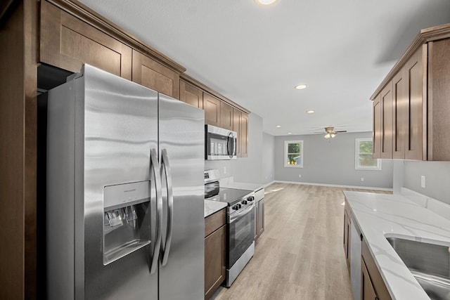 kitchen with sink, light hardwood / wood-style flooring, ceiling fan, light stone countertops, and appliances with stainless steel finishes