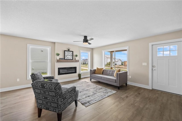 living area with a glass covered fireplace, wood finished floors, and baseboards