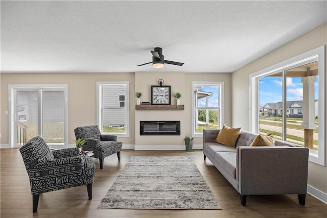 living area with a textured ceiling, ceiling fan, wood finished floors, baseboards, and a glass covered fireplace