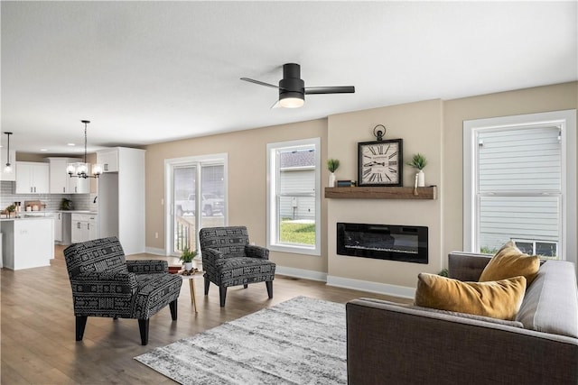 living room featuring ceiling fan with notable chandelier and light wood-type flooring