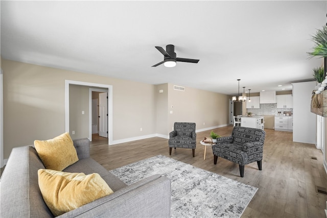 living room with ceiling fan with notable chandelier and light wood-type flooring