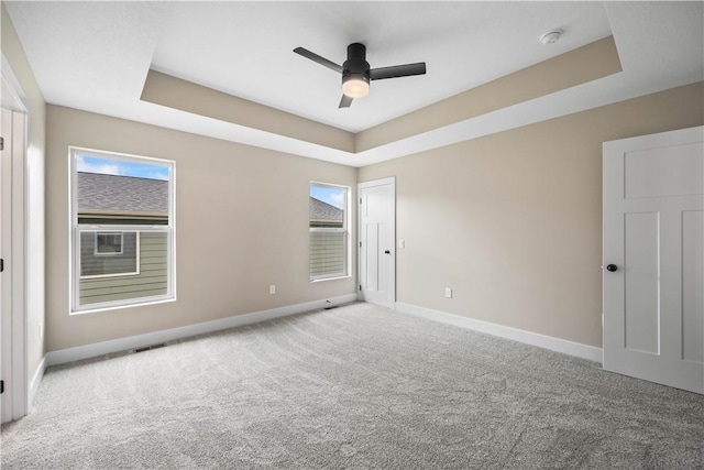 carpeted spare room with ceiling fan and a raised ceiling