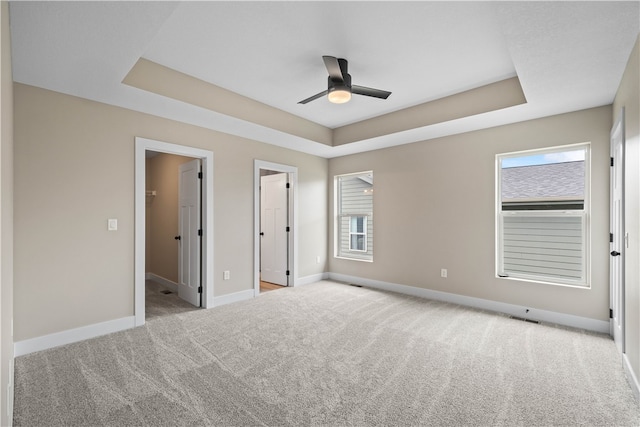 unfurnished bedroom featuring a spacious closet, light carpet, a raised ceiling, and ceiling fan