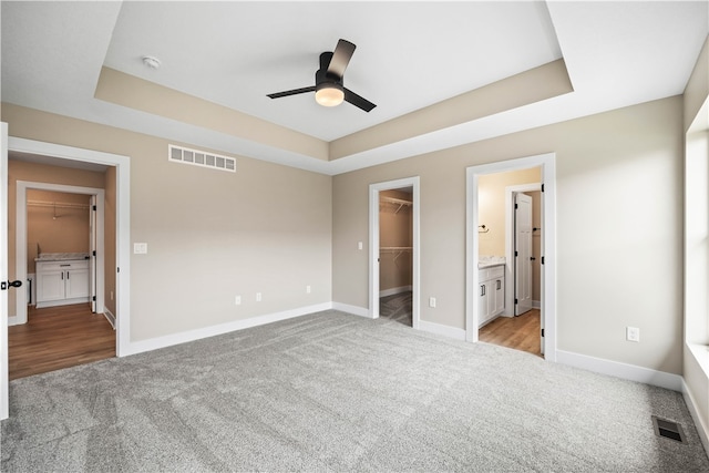 unfurnished bedroom with a closet, a spacious closet, ceiling fan, a tray ceiling, and light carpet