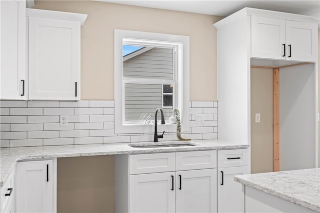 kitchen with sink, white cabinets, backsplash, and light stone countertops