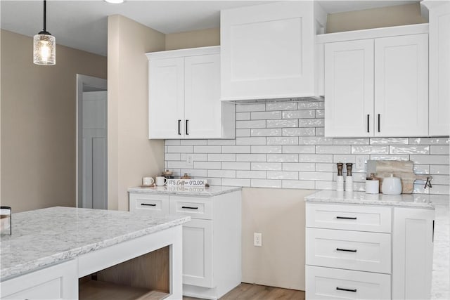 kitchen with white cabinets, pendant lighting, light hardwood / wood-style floors, backsplash, and light stone countertops