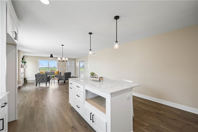 kitchen featuring an inviting chandelier, white cabinets, a center island, light stone counters, and dark hardwood / wood-style floors