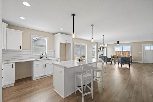 kitchen featuring decorative backsplash, white cabinetry, a sink, light stone countertops, and light wood-type flooring