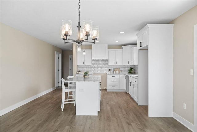 kitchen with a center island, decorative backsplash, white cabinetry, light wood-type flooring, and a kitchen breakfast bar