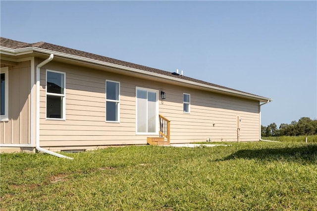 back of property with entry steps, roof with shingles, and a yard