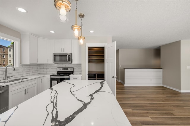 kitchen featuring white cabinets, stainless steel appliances, hanging light fixtures, dark wood-type flooring, and sink