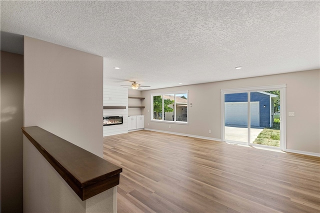 unfurnished living room featuring a textured ceiling, a fireplace, light wood-type flooring, and ceiling fan