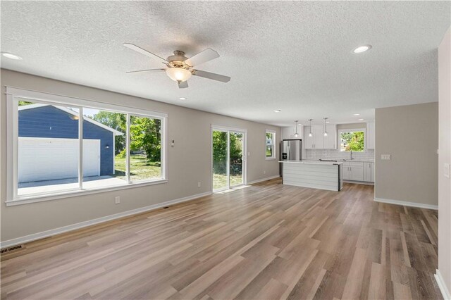 unfurnished living room with ceiling fan, sink, light hardwood / wood-style floors, and a textured ceiling