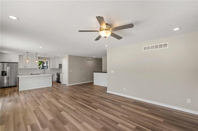 unfurnished living room featuring ceiling fan, a textured ceiling, hardwood / wood-style flooring, and sink