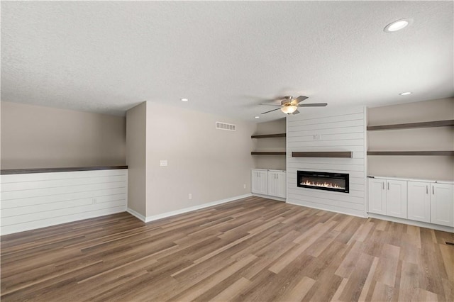 unfurnished living room featuring visible vents, light wood-style floors, a large fireplace, ceiling fan, and a textured ceiling