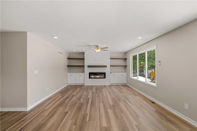 unfurnished living room with a large fireplace, light wood finished floors, baseboards, visible vents, and a textured ceiling