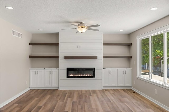 unfurnished living room featuring light wood finished floors, visible vents, a large fireplace, a textured ceiling, and baseboards