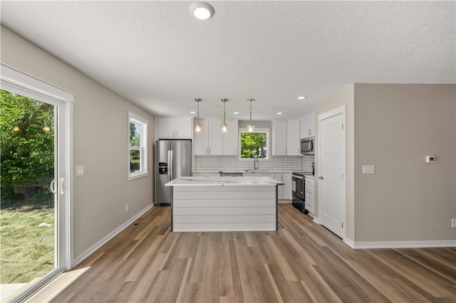 kitchen featuring appliances with stainless steel finishes, white cabinetry, light hardwood / wood-style floors, and a kitchen island