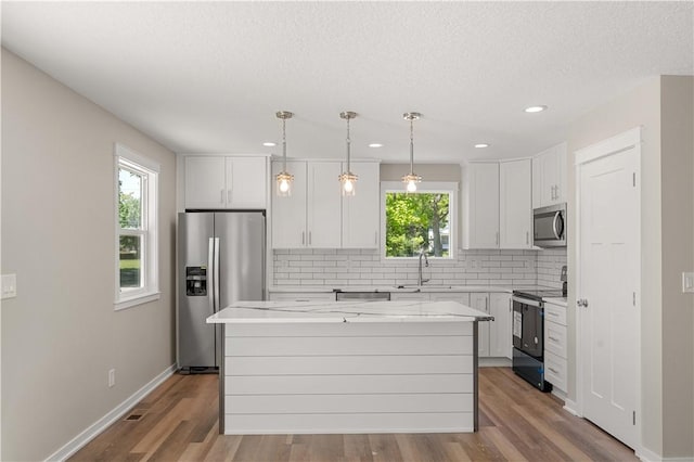 kitchen featuring light stone countertops, white cabinetry, stainless steel appliances, and a center island