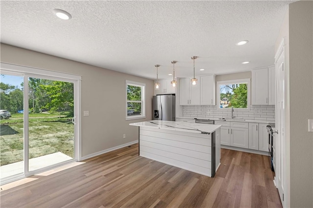 kitchen featuring a sink, a kitchen island, white cabinets, appliances with stainless steel finishes, and pendant lighting