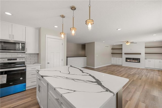 kitchen featuring a large fireplace, white cabinets, a kitchen island, hanging light fixtures, and stainless steel appliances