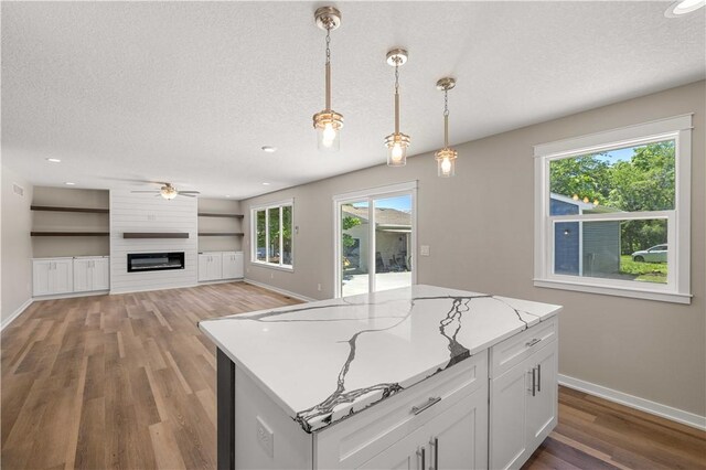 kitchen featuring decorative light fixtures, a large fireplace, hardwood / wood-style floors, white cabinets, and a textured ceiling