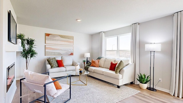 living area with a glass covered fireplace, light wood-style floors, baseboards, and a textured ceiling