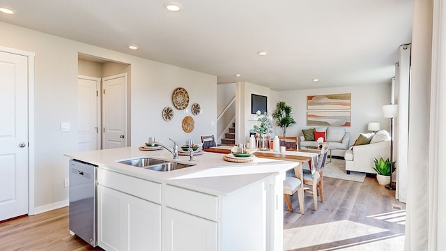 kitchen featuring dishwasher, an island with sink, sink, light wood-type flooring, and white cabinets