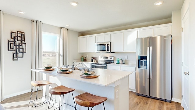 kitchen with light hardwood / wood-style flooring, stainless steel appliances, white cabinetry, sink, and an island with sink