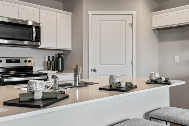 kitchen featuring white cabinets, light stone counters, stainless steel appliances, sink, and a breakfast bar