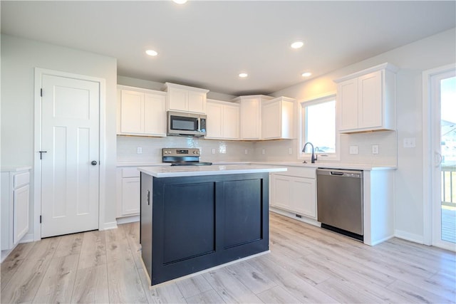 kitchen with decorative backsplash, light wood-type flooring, stainless steel appliances, a center island, and white cabinetry