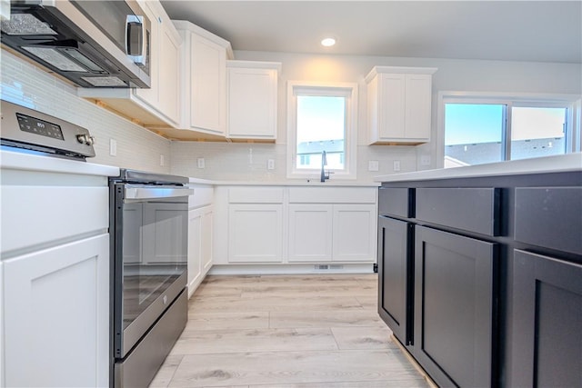 kitchen featuring sink, light hardwood / wood-style flooring, decorative backsplash, appliances with stainless steel finishes, and white cabinetry