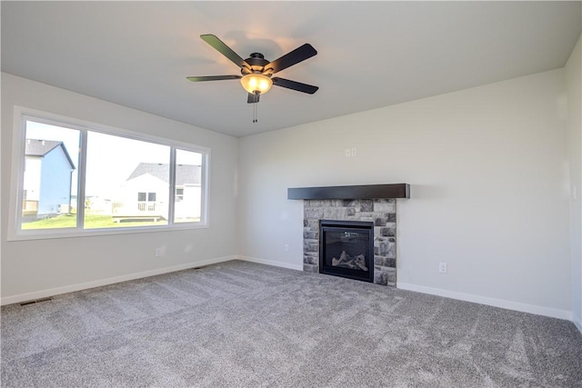 unfurnished living room featuring carpet, a stone fireplace, and ceiling fan