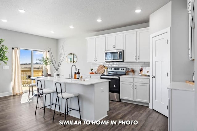 kitchen with a kitchen bar, a center island with sink, white cabinets, and appliances with stainless steel finishes