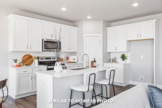 kitchen with white cabinetry, stainless steel appliances, sink, and a kitchen island with sink