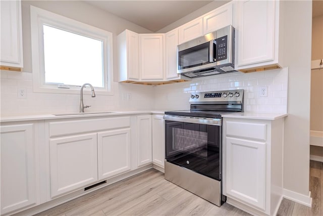 kitchen with stainless steel appliances, sink, white cabinets, and light hardwood / wood-style flooring