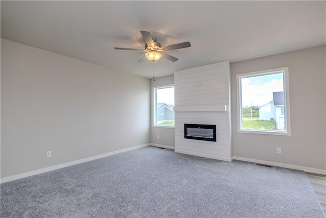 unfurnished living room featuring a large fireplace, ceiling fan, and plenty of natural light