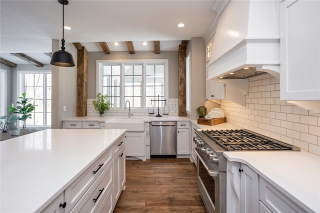 kitchen with appliances with stainless steel finishes, custom range hood, dark wood-type flooring, beam ceiling, and decorative light fixtures