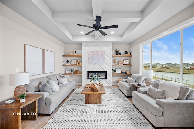 living room with ceiling fan, a fireplace, a water view, light hardwood / wood-style flooring, and beam ceiling