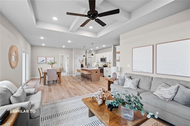 living room with sink, ceiling fan, beamed ceiling, light hardwood / wood-style flooring, and a tray ceiling